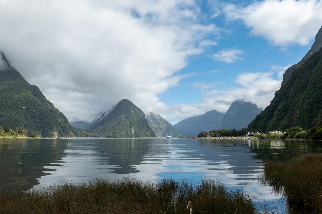 Still water reflecting green mountain peaks under drifting clouds