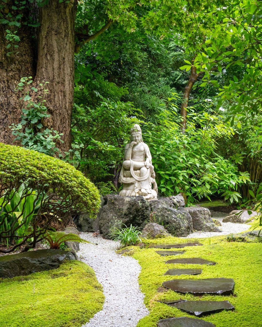 A moss garden path leading to a stone statue in Japan